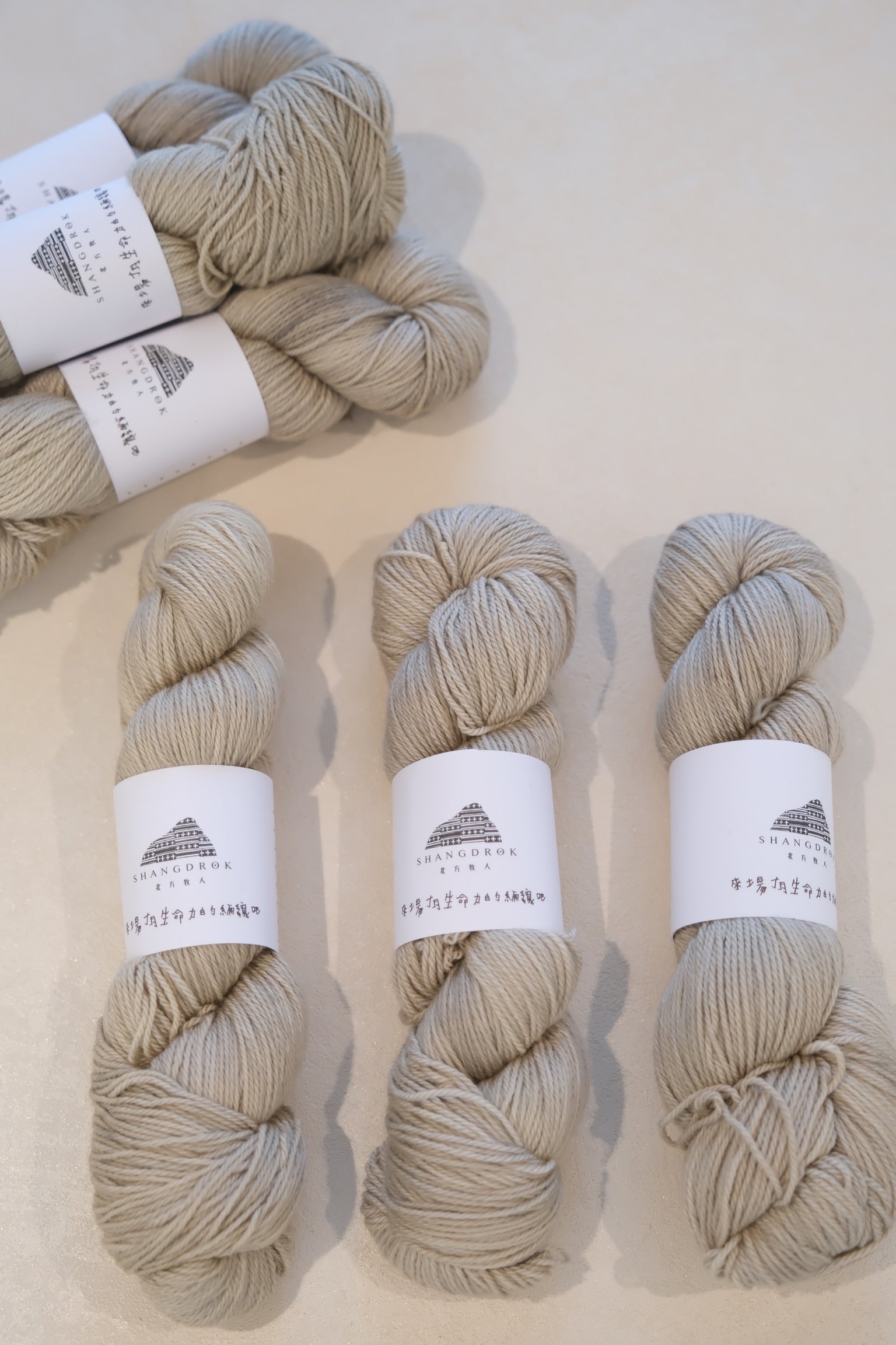 Four skeins of beige yarn with labels on a light background