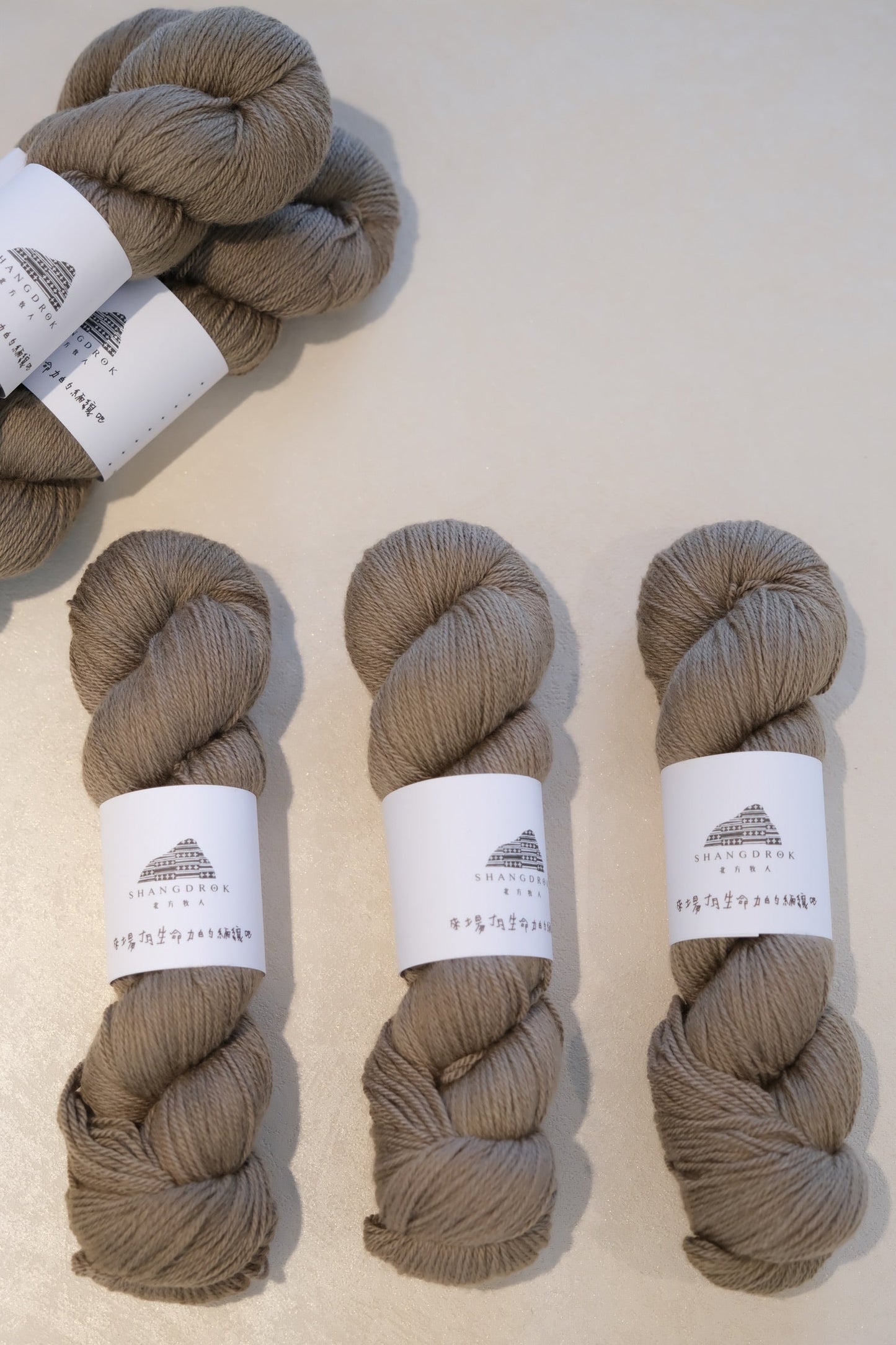 Four skeins of brown yarn with labels on a light beige background